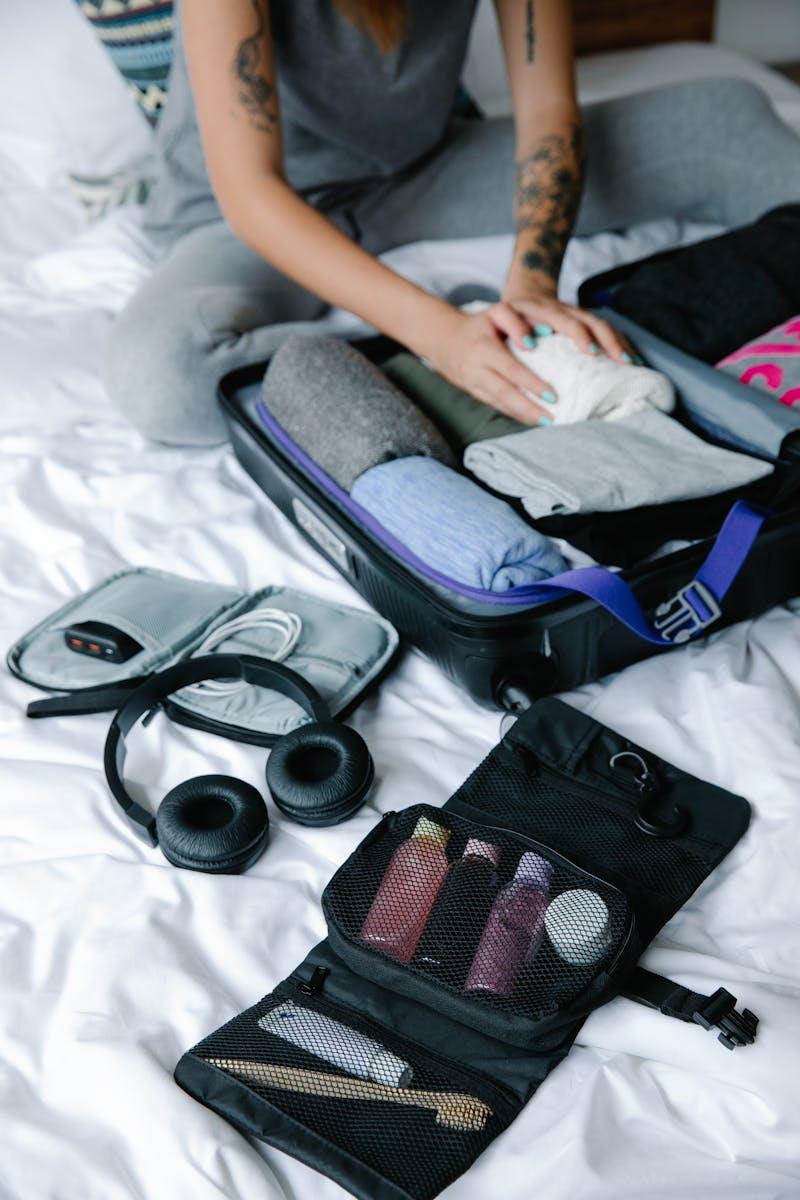 Photo by Timur Weber Person organizing suitcase with clothes and toiletries on bed, preparing for travel.