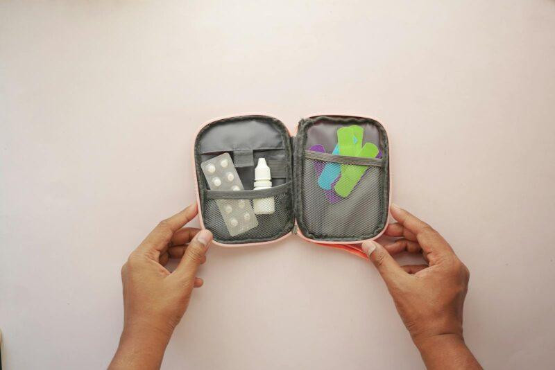 Travel First Aid Kits: Essential Items Every Traveler Needs 5 Open first aid kit containing band aids, tablets, and medicines, held by hands.