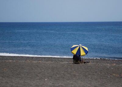 Black sand beach with sea, single lounge chair with blue and yellow umbrella