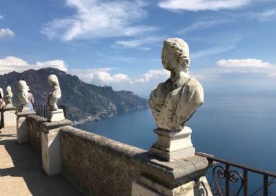 Busts lining balcony railing/wall with view of sea